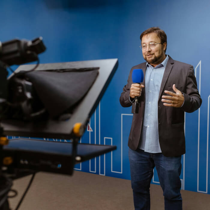 Journalist steht mit blauer Wand vor der Kamera und berichtet.